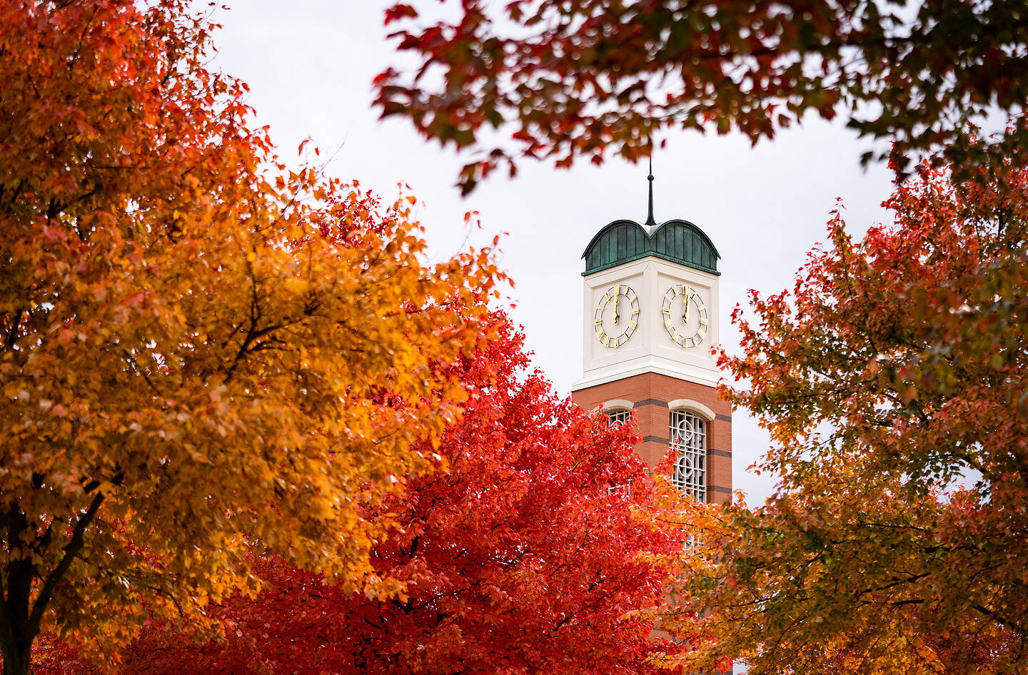 A clock tower framed by vibrant autumn foliage in shades of red, orange, and yellow.